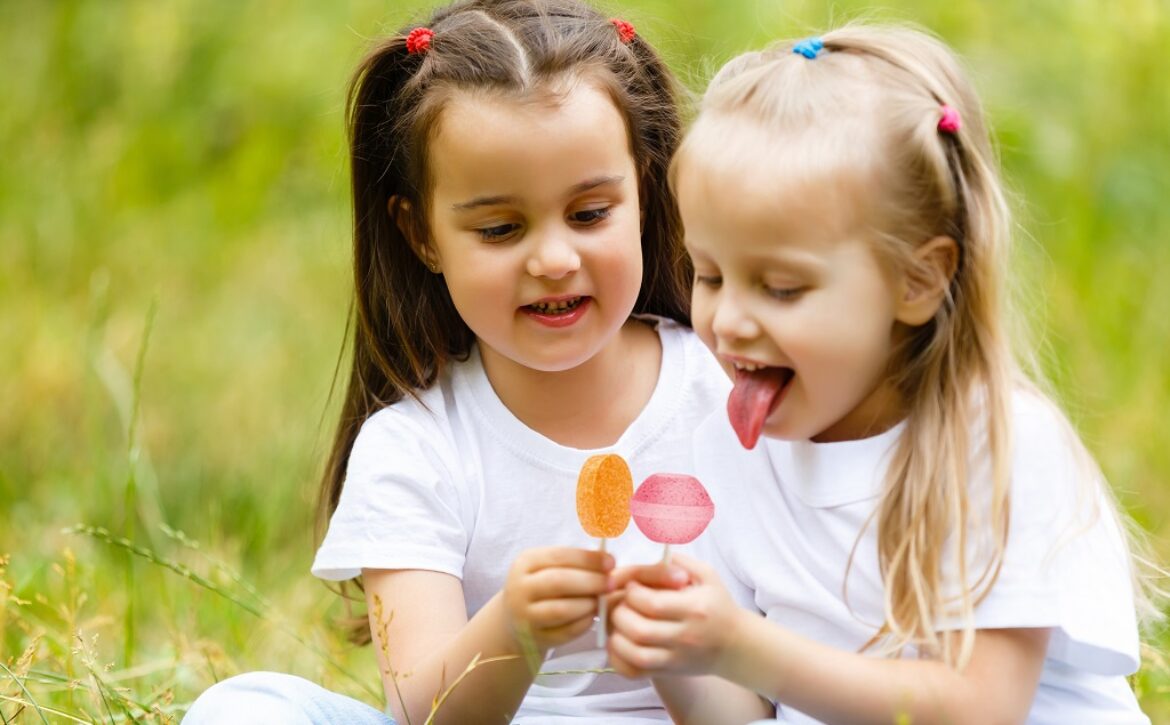 Two cute little sisters eating huge lollipops outdoors on beautiful summer day